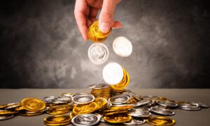 hand dropping gold and silver coins onto a pile on a table