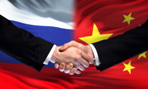 china and russia flags in background with handshake happening in foreground