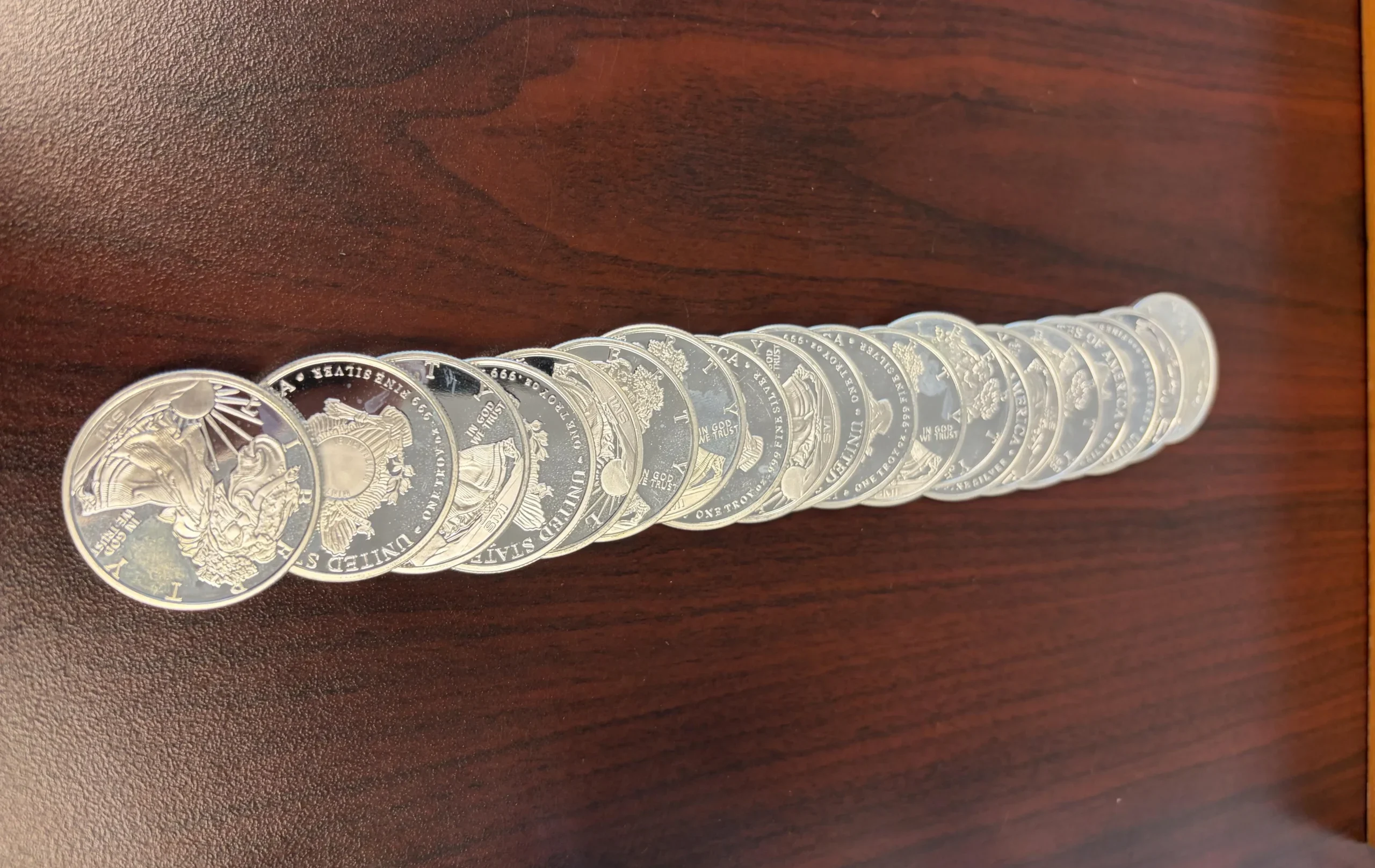 shiny silver coins lined up on a dark wooden table | Metals Edge shiny silver coins lined up on a dark wooden table