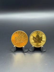 Stacked Gold Coins | Metals Edge | Metals Edge Two Canadian gold coins with maple leaf design on display stands against a dark background, side by side.
