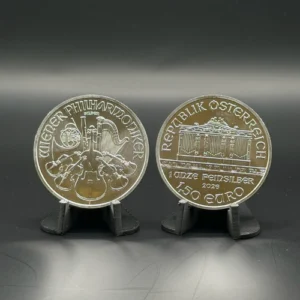 1 oz Austrian Silver Philharmonic | Metals Edge Two Austrian silver coins on display stands; left coin shows orchestral instruments with 'Wiener Philharmoniker' inscription, right coin shows the Austrian Parliament Building and 'Republik Österreich' with 150 Euro value.